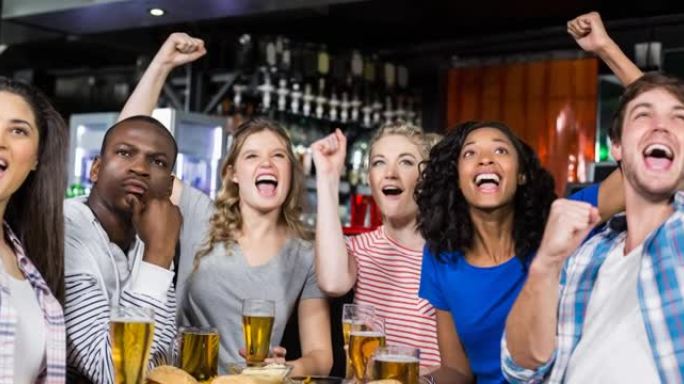 快乐的男女体育迷在酒吧观看比赛，欢呼和喝酒