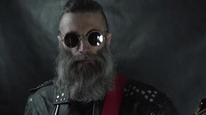 留着胡须的摇滚音乐家头部特写，剃光的太阳穴戴着圆形眼镜和皮夹克
