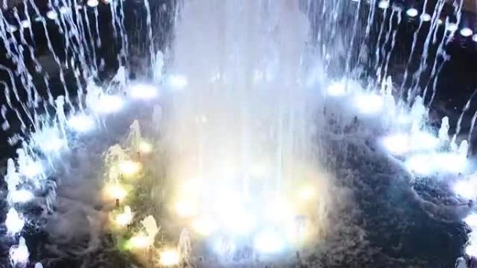喷泉的碎片。水流以不同的节奏上升，下降，从水下的灯发出多色照明。