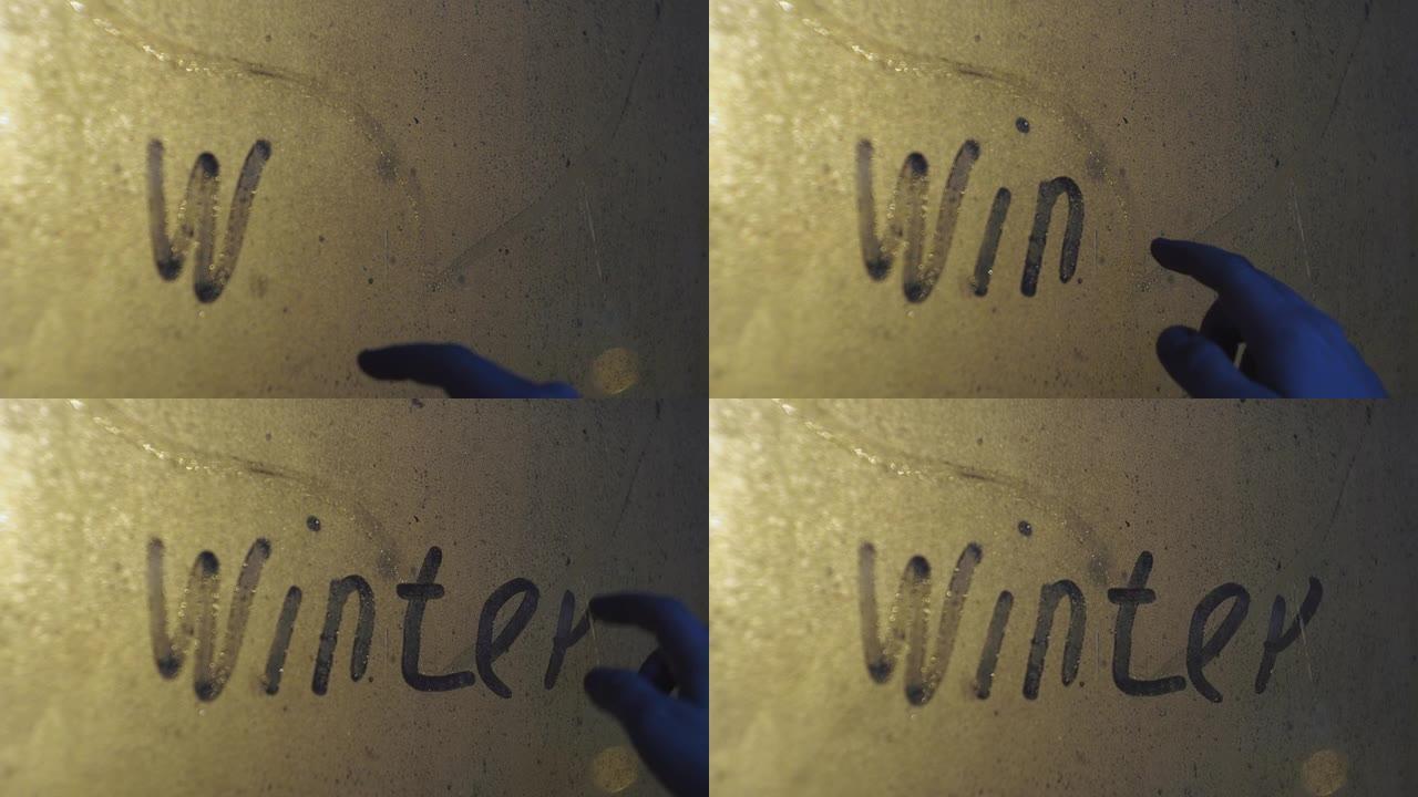 一只手在雾蒙蒙的窗户上写下冬天这个词。玻璃后面正在下雪。照亮路灯。夜间暴风雪
