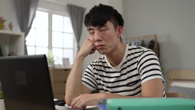 特写镜头日本大学生男孩带着无聊的脸看着空旷的地方和旋转笔，同时在家学习观看在线视频讲座。