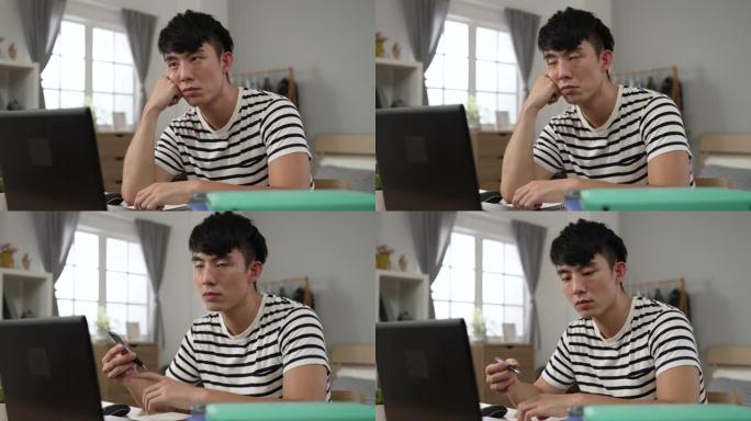 特写镜头日本大学生男孩带着无聊的脸看着空旷的地方和旋转笔，同时在家学习观看在线视频讲座。