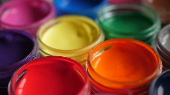 将水粉画颜料放在罐子里明亮的颜色特写。塑料罐上的多色水粉旋转套装。旋转多色背景。多色油漆的背景。创意