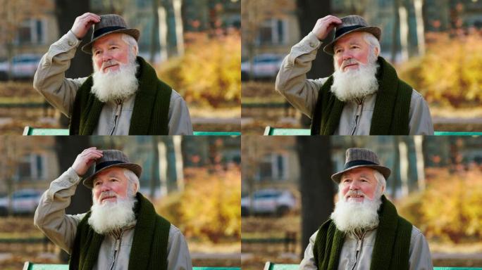 公园里戴着老式帽子的迷人老人脱下帽子，然后在深秋的日子里坐下