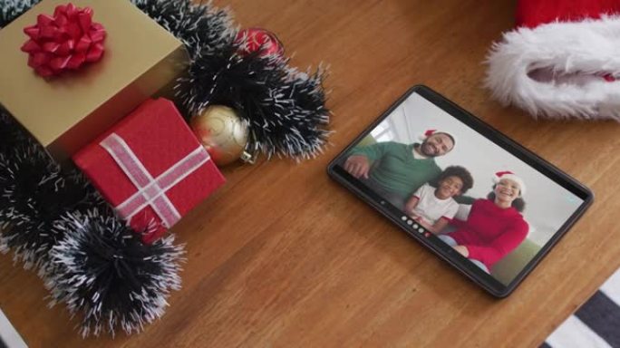 在平板电脑上的圣诞节视频通话中戴着圣诞老人帽子的微笑的非裔美国人家庭