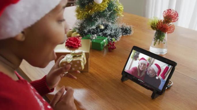 戴着圣诞老人帽子的非洲裔美国妇女使用平板电脑进行圣诞视频通话，屏幕上有情侣