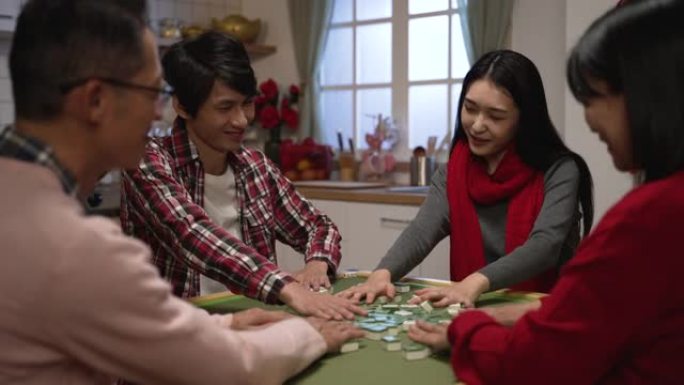 亚洲家庭成员看着对方狡黠的微笑，而洗牌麻将在桌上。除夕在家里通宵玩游戏