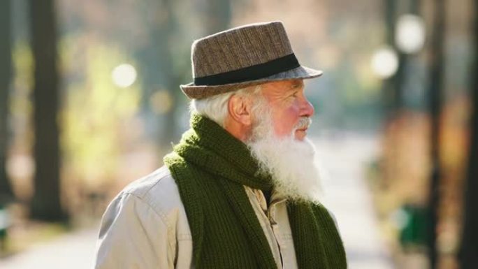 公园里的秋天有魅力的老人戴着帽子在镜头前摆姿势散步，呼吸新鲜空气