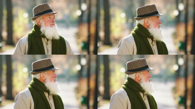 公园里的秋天有魅力的老人戴着帽子在镜头前摆姿势散步，呼吸新鲜空气