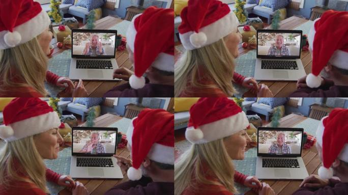 白人夫妇戴着圣诞老人的帽子，使用笔记本电脑与屏幕上的男人进行圣诞节视频通话