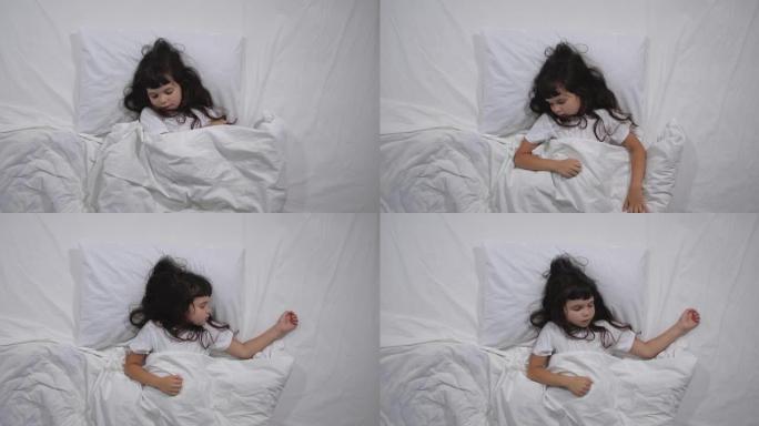 6岁的小女孩的俯视图，长长的棕色头发在床上睡着了，白色床单在明亮的房间里。高角度拍摄。学龄前女孩要睡