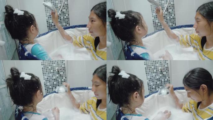 亚洲女孩淋浴她的姐姐的脸，同时放松在塑料浴缸一起在家里，生活方式的概念。