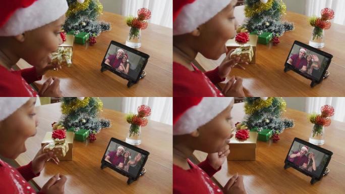 戴着圣诞老人帽子的非洲裔美国妇女使用平板电脑进行圣诞视频通话，屏幕上有情侣
