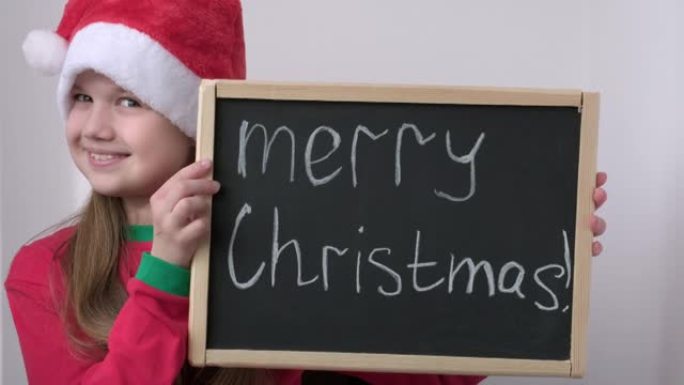 可爱的小圣诞老人助手女孩显示广告牌与文字圣诞快乐。戴着红色圣诞老人帽子的可爱的孩子拿着黑板。新年促销