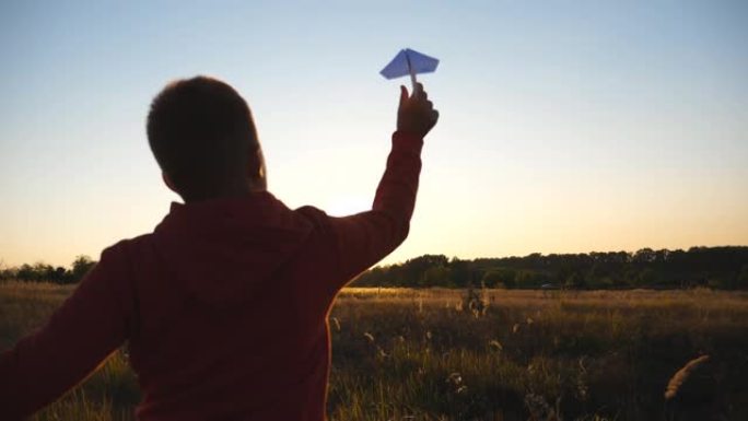 跟随可爱的小孩，用纸飞机在草地上慢跑。无忧无虑的男孩沿着草地奔跑，在日落背景下发射玩具飞机。童年梦想