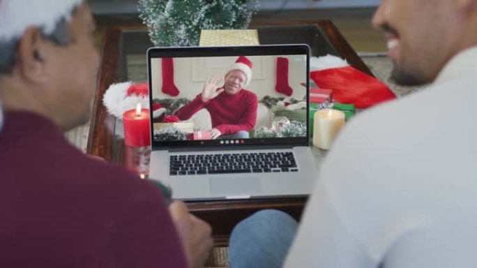 微笑的混血儿父子使用笔记本电脑与屏幕上的男人进行圣诞节视频通话