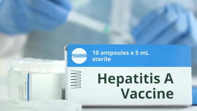 桌上装有甲型肝炎疫苗的盒子，可对抗模糊的实验室助理或医生。虚构的phaceutical徽标