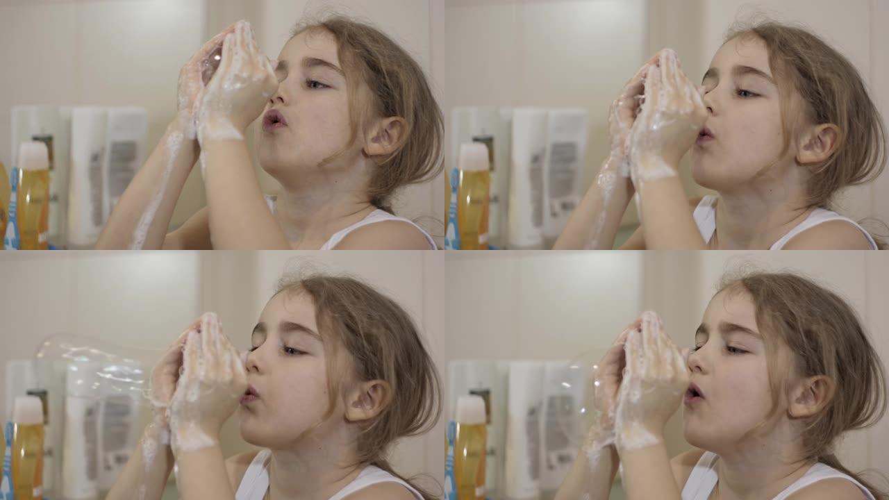 肖像年轻有趣的小女孩在浴室里吹肥皂泡看着镜子反射。快乐可爱的高加索无牙儿童顽皮女孩浴室有鳍吹肥皂泡