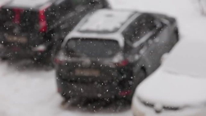 阴天，缓慢的雪落在停放的汽车的模糊背景上，有选择性的焦点