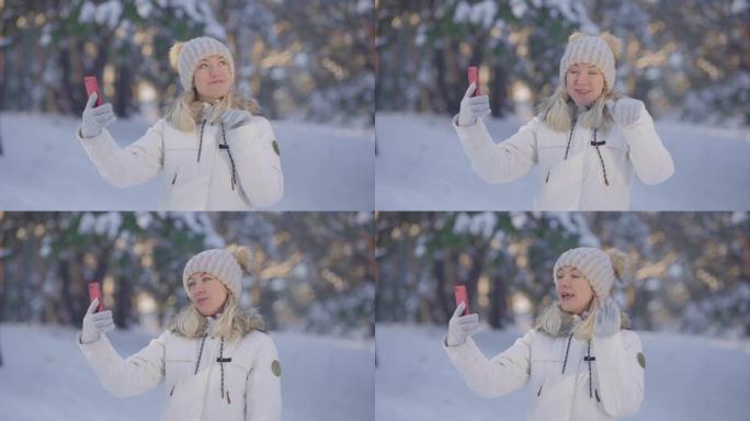 穿着温暖的冬装可爱的女孩的肖像，用手机聊天，欢欣鼓舞。年轻女子在白雪皑皑的森林模糊背景下在户外摆姿势