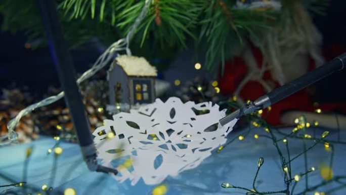 用于显微外科手术的机器人机械手握住并拉伸纸雪花。模糊背景下的圣诞树和装饰品。特写。