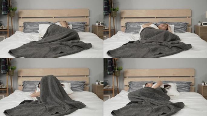 亚洲女性躺在床上醒来翻来覆去，由于家里现代卧室的床垫质量不好，感到不适。