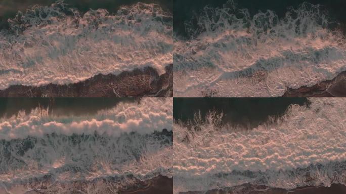 强大的海浪撞击岩石。海浪飞溅并产生白色泡沫。日落时暴风雨般的大海。戏剧性的泡沫波在岩石海滩上破裂。大