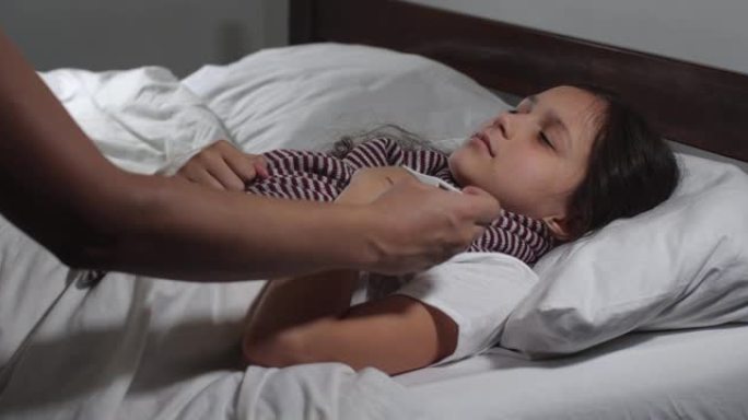 9岁小女孩的特写镜头感冒躺在床上患流感。小孩咳嗽和打喷嚏，母亲的手检查她的体温，抚摸额头。4K