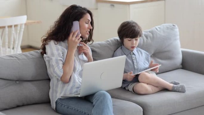在家工作的多任务妈妈打电话帮助学龄前的儿子在平板电脑上在家上学
