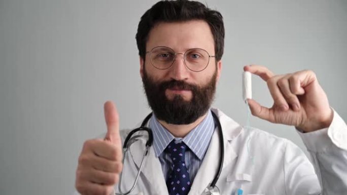 一位男性妇科医生赞成在女性月经期间使用棉花糖。穿着白大褂和眼镜的医生谈到需要使用卫生棉条。