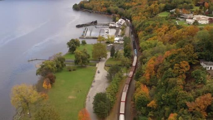 在一个美丽的日子里，纽约哈德逊的康沃尔郡高视角，有五颜六色的秋叶和一列长长的货运列车。