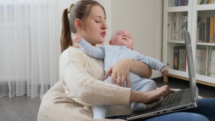 忙碌的自由职业母亲在家庭办公室用笔记本电脑工作，抱着哭泣的儿子