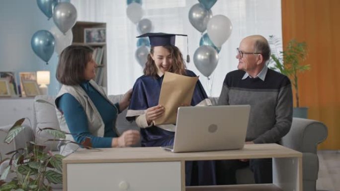 高中毕业，快乐的父母祝贺女毕业生毕业，并在一个在线仪式上向她颁发文凭，她坐在家里的客厅里，拿着气球