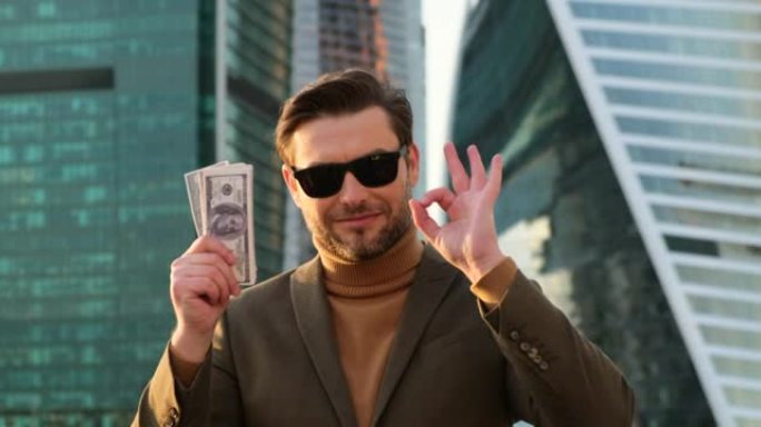 一个穿着西装和太阳镜的男人向相机展示了美元。年轻的百万富翁