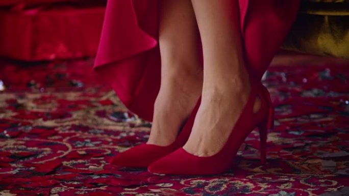 特写，一位穿着红色连衣裙的女士穿上红色鞋子，坐在酒店房间的扶手椅上，一位女士正在为圣诞节的假期做准备