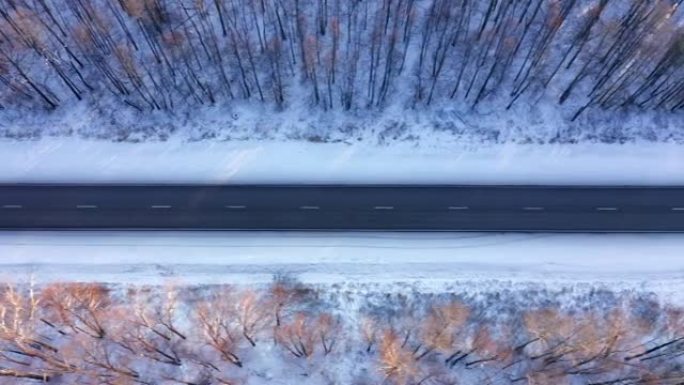从一条穿过白雪覆盖的森林边缘的空轨道上方观看。周游全国的概念。一条柏油路连接着不同的区域。