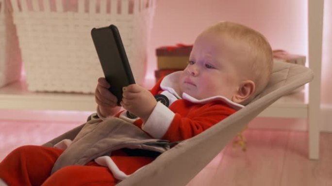 孩子穿着圣诞老人玩手机玩得开心，快乐的孩子看着智能手机屏幕庆祝他的第一个新年。