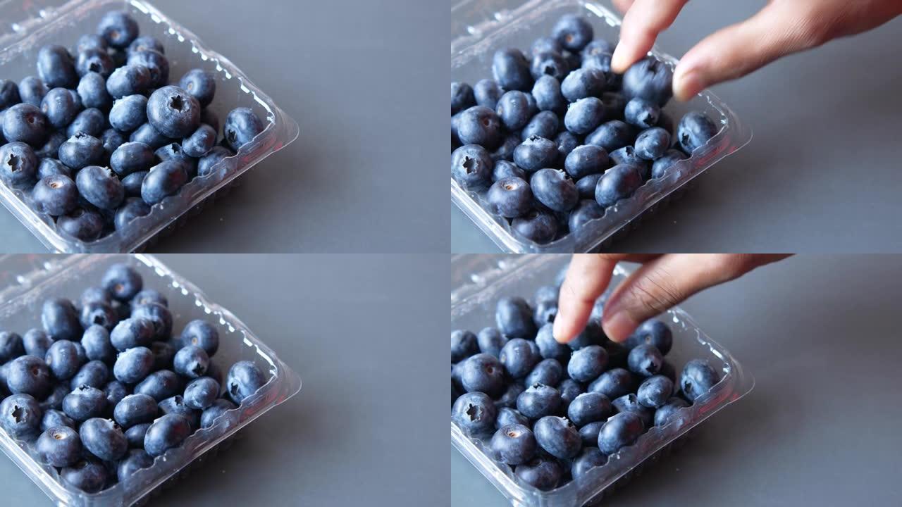 从桌子上的塑料盒中手工采摘蓝色浆果
