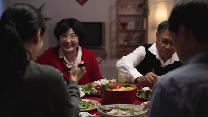 选择性聚焦，肩视微笑的亚洲老年夫妇祖父和祖母在新年前夕用筷子拿着食物，在餐桌上给他们的儿媳妇