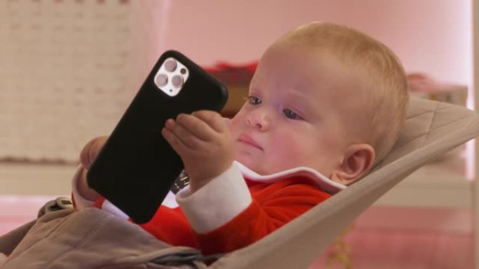 孩子穿着圣诞老人玩手机玩得开心，快乐的孩子看着智能手机屏幕庆祝他的第一个新年。