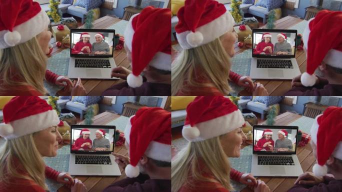 微笑的高加索夫妇戴着圣诞老人的帽子，使用笔记本电脑与家人在屏幕上进行圣诞节视频通话