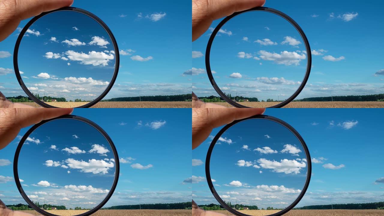 偏光滤镜的视觉效果以夏季乡村美丽的云彩为例。手握一个圆形滤光片，应用偏振效应。