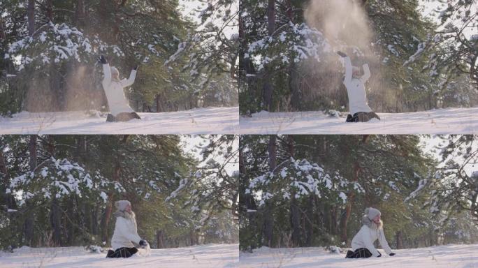 穿着温暖的冬装的快乐可爱女孩坐在雪地里，玩得开心，扔起来，开心地笑。阳光明媚的冬天下雪的乐趣。松林白