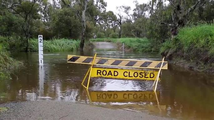 在澳大利亚农村地区，一条道路封闭的标志坐落在一条被洪水淹没的小溪道口前。