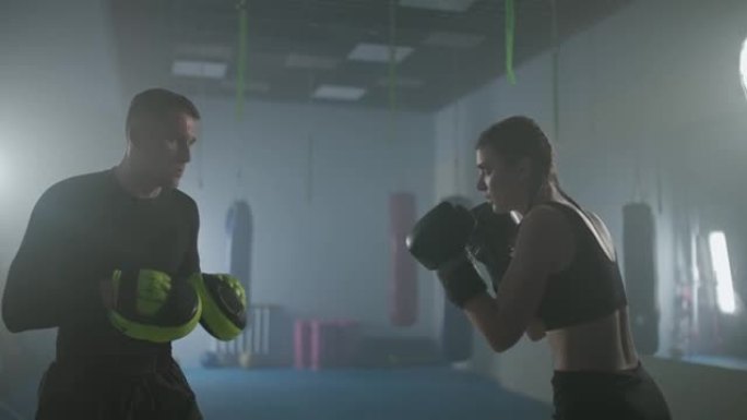 年轻的女战士训练他的快拳，打焦点手套，在拳击馆与一名男教练一起训练一天，年轻的女战士快速出击。