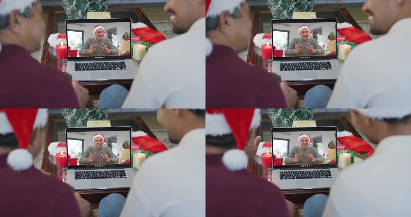 带有圣诞老人帽子的混血儿父亲和儿子使用笔记本电脑进行圣诞节视频通话，屏幕上有男人