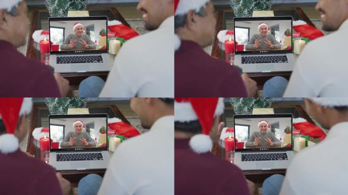 带有圣诞老人帽子的混血儿父亲和儿子使用笔记本电脑进行圣诞节视频通话，屏幕上有男人