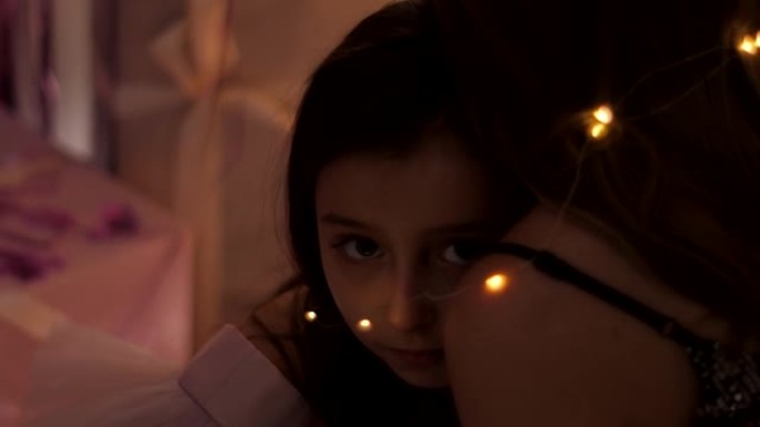 女孩躺在母亲的肩膀上，绑着花环，看着圣诞节的镜头之夜