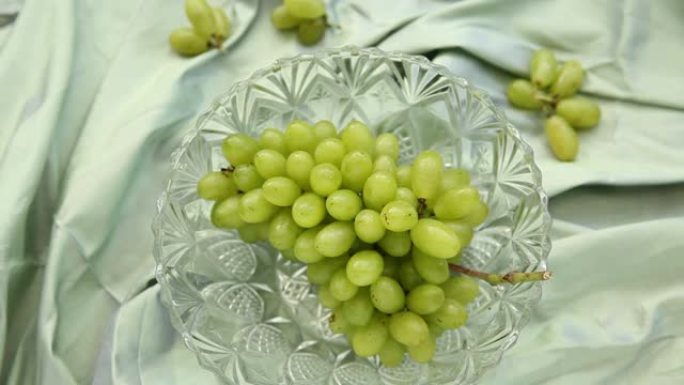 泰国丝绸织物桌子覆盖水晶碗中的绿色葡萄，自然光背景