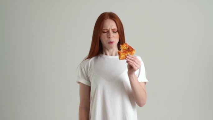 饥饿沮丧的年轻女子的肖像，食欲不佳，吃披萨，对食物质量不满意，胃痛。